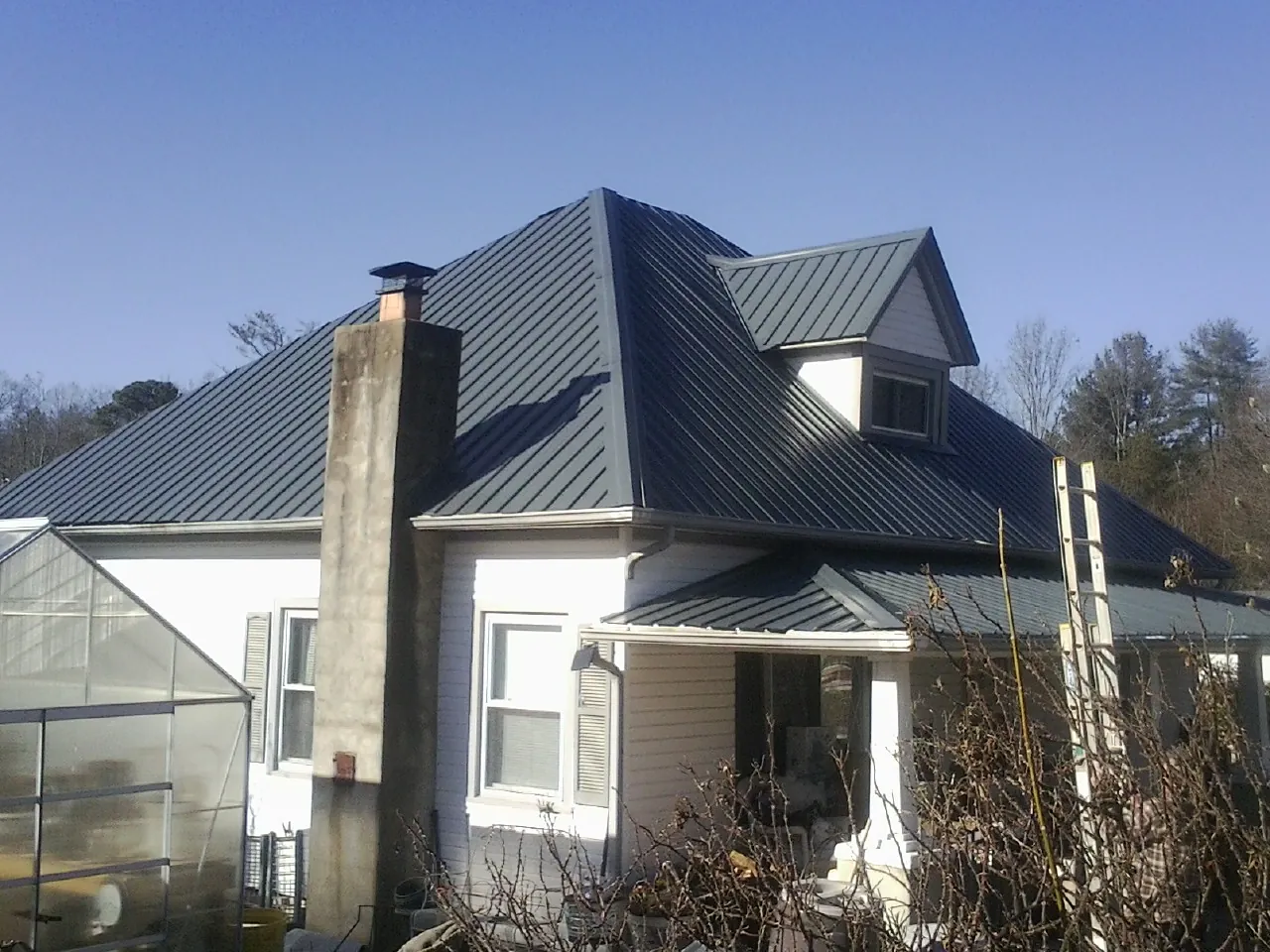 Dark blue standing seam metal roof on a white farmhouse with dormer — Slate & Tile Roof Repair by Roofing Brothers in Mohler