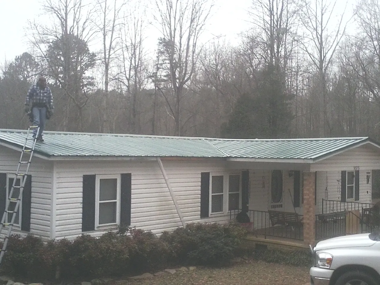 Worker on a ladder beside a new green metal roof on a ranch home in Mohler