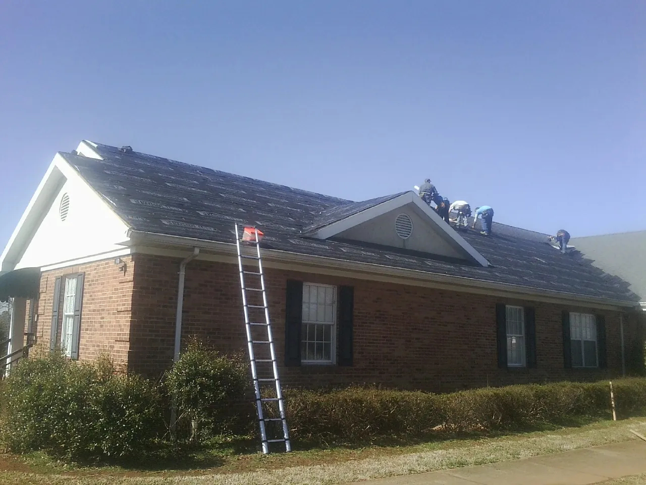 Crew tearing shingles off a brick ranch roof with a ladder set — Metal Roof Repair work by our crew in Mohler
