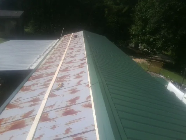 Old rusted panels beside newly installed green metal roofing — Wind Damage Roof Repair by Roofing Brothers in Mohler