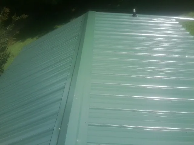 New green metal panels meeting at the ridge of a roof — Flat Roof Repair work by our crew in Mohler