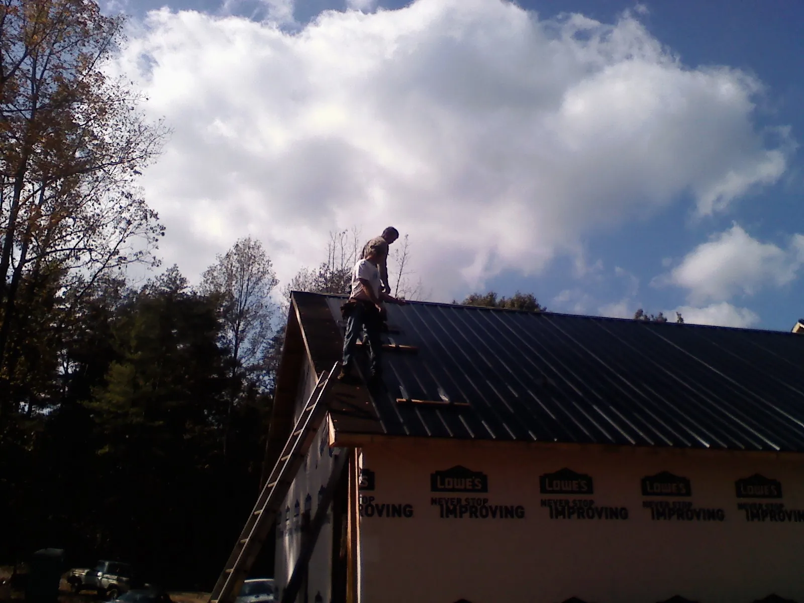 Roofer fastening dark metal panels high against a cloudy sky, from a Roof Inspection job in Mohler
