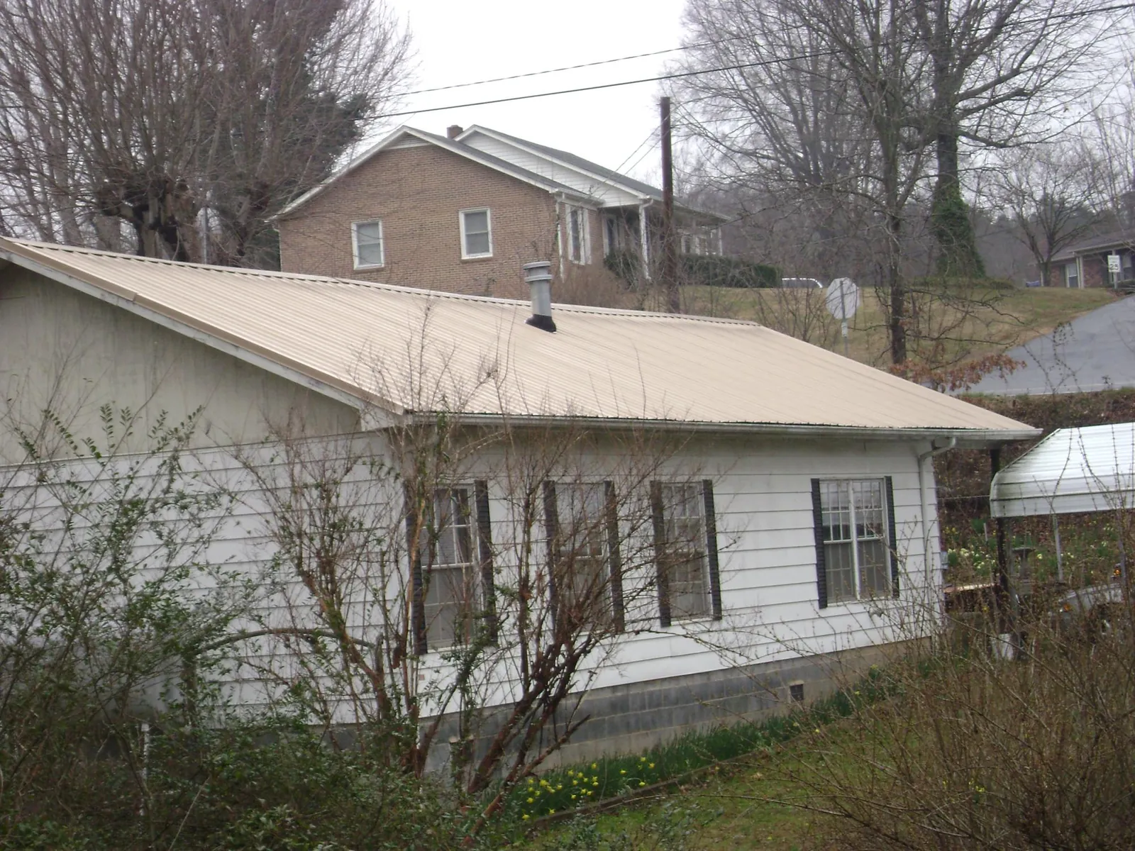 Tan metal roof on a white sided house set into a hillside — Commercial Roofing by Roofing Brothers in Mohler