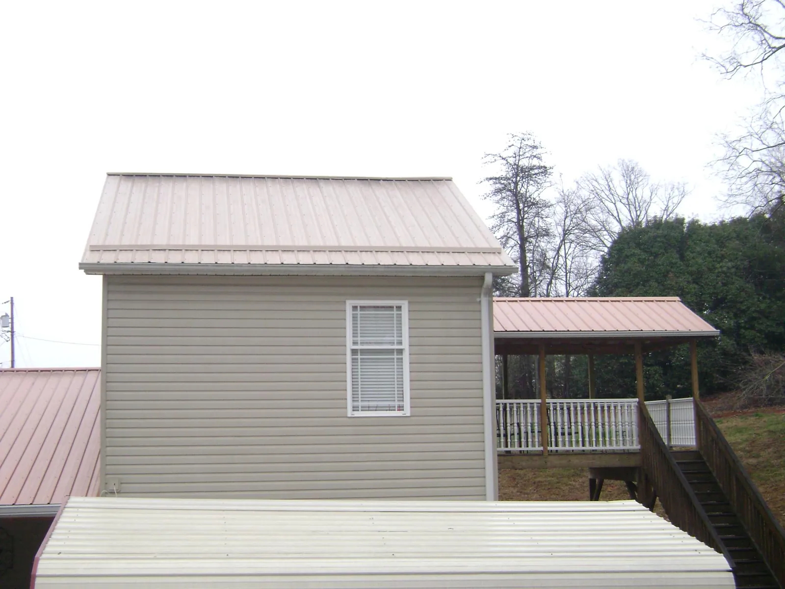 Tan metal roofs on a two story addition and attached porch, from a Roof Replacement job in Mohler